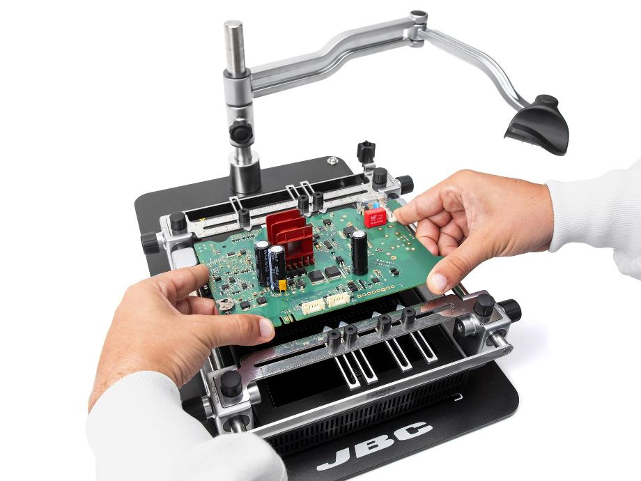 Hands placing a PCB in the PCB rework bench from JBC